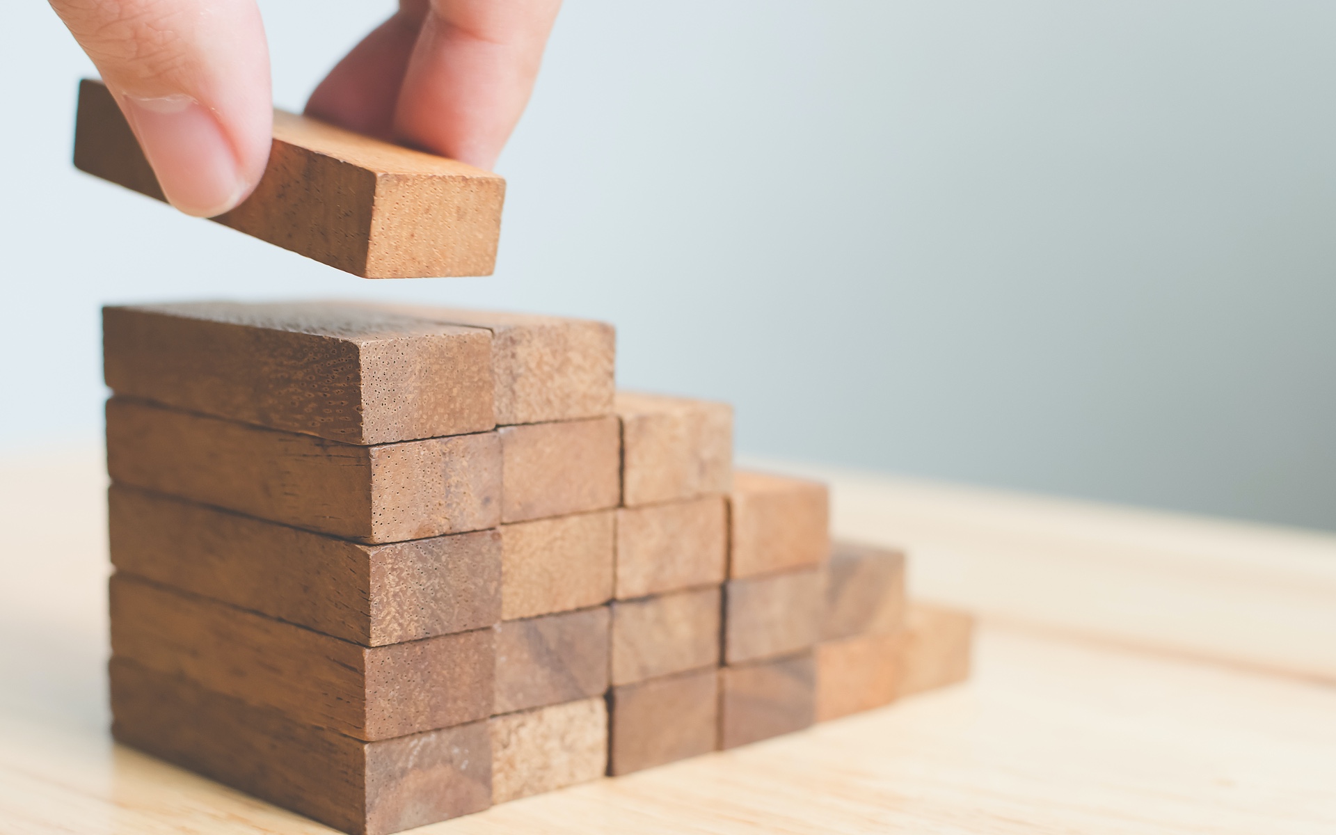 Various wodden blocks being stacked on top of each other by someone's hand, forming stairs going up.